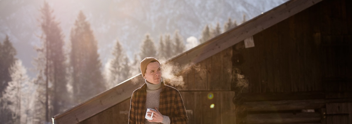 Mann mit Teetasse vor Hütte im Schnee