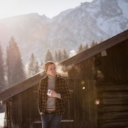 Mann mit Teetasse vor Hütte im Schnee